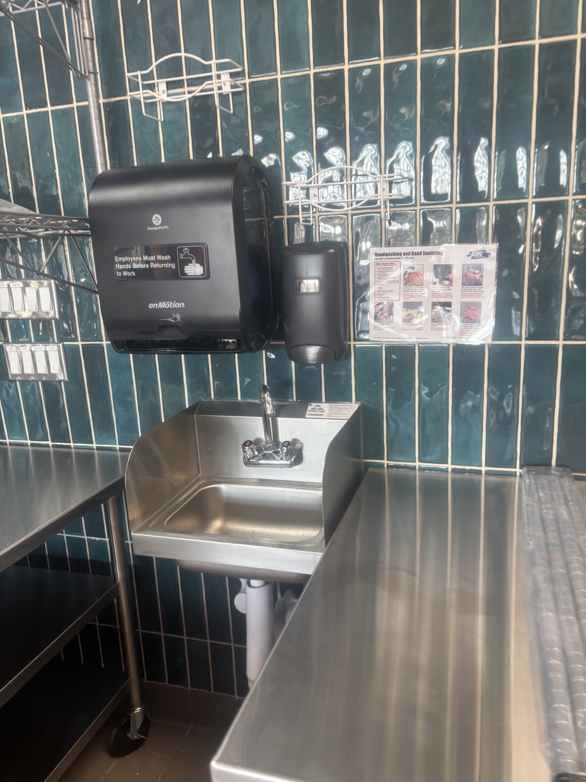 Clean stainless steel handwashing sink and work surfaces in a tiled restaurant space